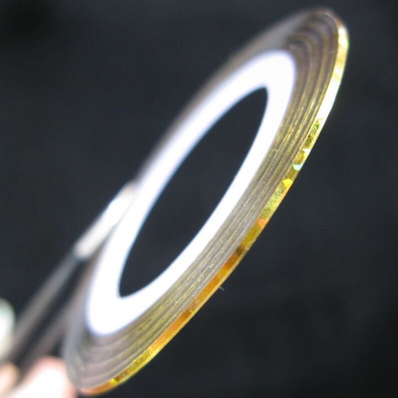 May include: Gold nail art tape with a white backing. The tape is rolled up and the gold side is facing the camera.