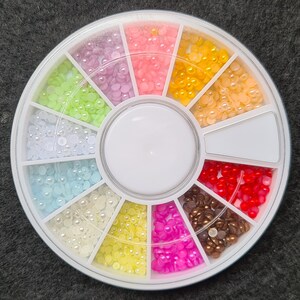 Pode incluir: Uma roda de pl&aacute;stico branca com 12 compartimentos, cada um cheio de pequenas contas de cor p&eacute;rola. As contas s&atilde;o dispostas em um padr&atilde;o circular, com cada compartimento contendo uma cor diferente. As cores incluem branco, azul claro, rosa claro, amarelo, verde claro e vermelho.