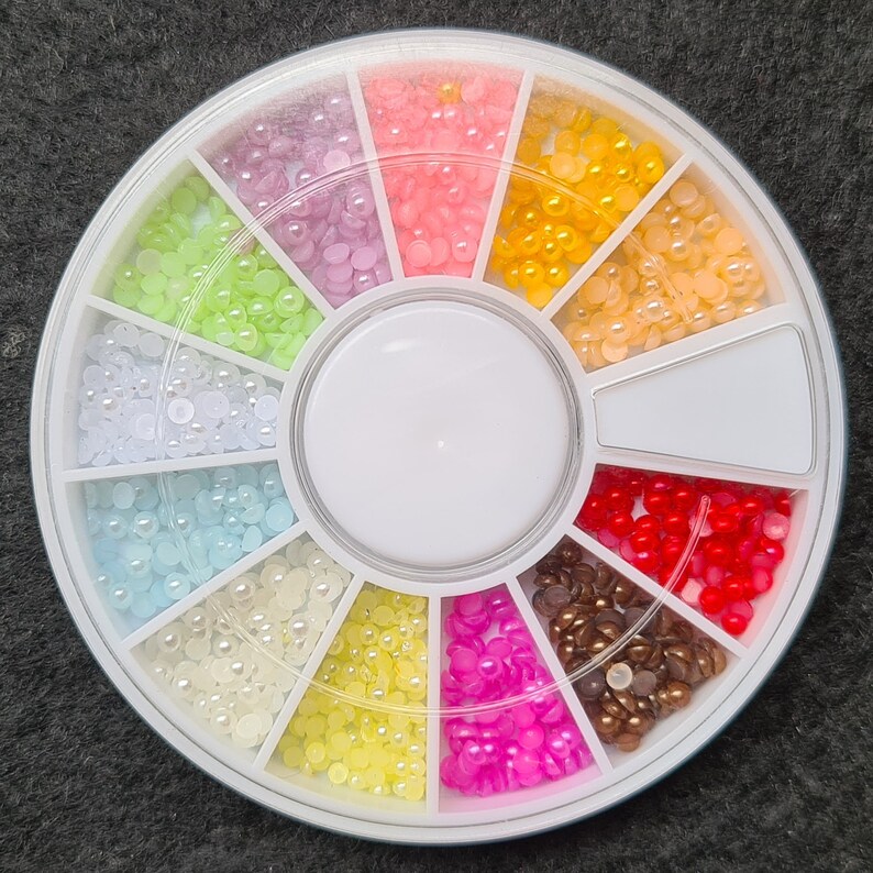 Pode incluir: Uma roda de pl&aacute;stico branca com 12 compartimentos, cada um cheio de pequenas contas de cor p&eacute;rola. As contas s&atilde;o dispostas em um padr&atilde;o circular, com cada compartimento contendo uma cor diferente. As cores incluem branco, azul claro, rosa claro, amarelo, verde claro e vermelho.