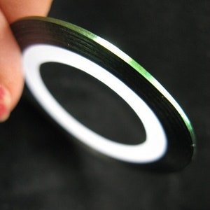 May include: A roll of black and green nail art tape with a white stripe in the center.