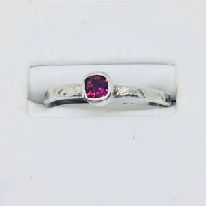 May include: A silver ring with a textured band and a square-shaped pink gemstone.