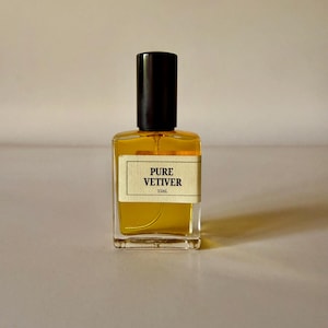 Può includere: Un flacone in vetro rettangolare riempito di liquido dorato, dotato di un tappo cilindrico nero e di un'etichetta color crema con il testo nero PURE VETIVER e 15mL stampato sul davanti. Il flacone ha una base in vetro trasparente e un tubicino.