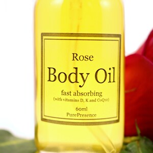 May include: A clear glass bottle of rose body oil with a gold label that reads "Rose Body Oil fast absorbing (with vitamins D, K and CoQ10) 60ml Pure Presence".