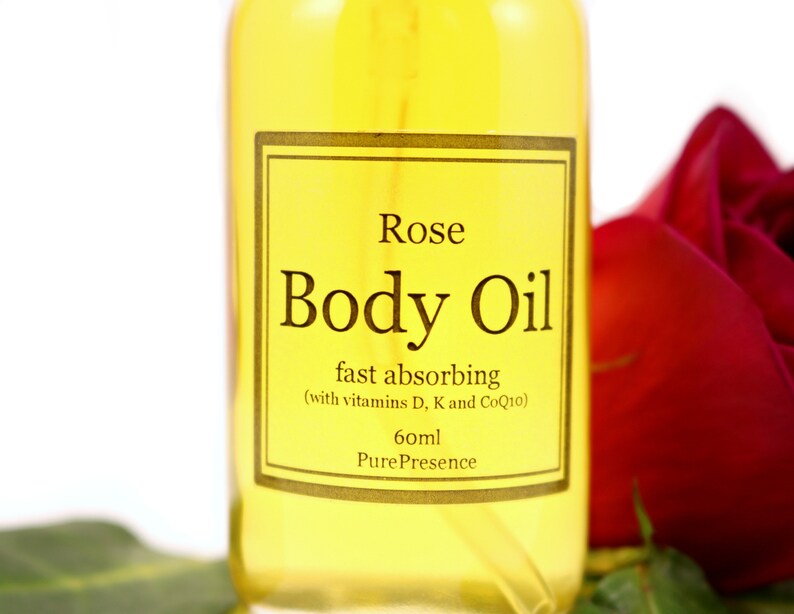 May include: A clear glass bottle of rose body oil with a gold label that reads "Rose Body Oil fast absorbing (with vitamins D, K and CoQ10) 60ml Pure Presence".