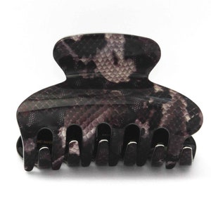 Peut inclure: Une pince à cheveux noire et grise avec un motif peau de serpent. La pince a quatre dents.