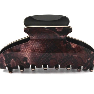 May include: A large black and brown hair claw with a snake skin pattern. The claw has a gold trim around the edge.