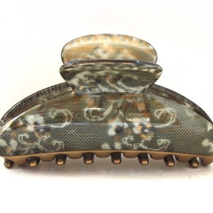 Op de afbeelding: Een grote, bruin en wit gepatroneerde haarspeld met een bronzen metalen basis en tanden.