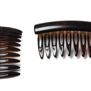 Op de afbeelding: Twee bruine plastic haar kammen. E&eacute;n kam heeft een gebogen handvat en een rij tanden. De andere kam heeft een recht handvat en een rij tanden.