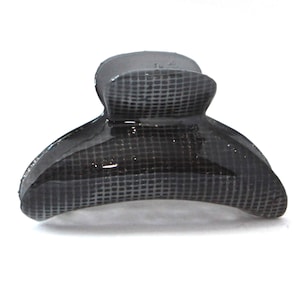 May include: A dark grey hair claw clip with a grid pattern. The clip is made of a glossy material and has a curved design. This hair accessory is suitable for various hairstyles and hair types.