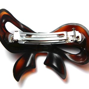 May include: A brown plastic hair clip shaped like a bow with a silver metal clasp. The clasp has the words "Made in Japan" engraved on it.