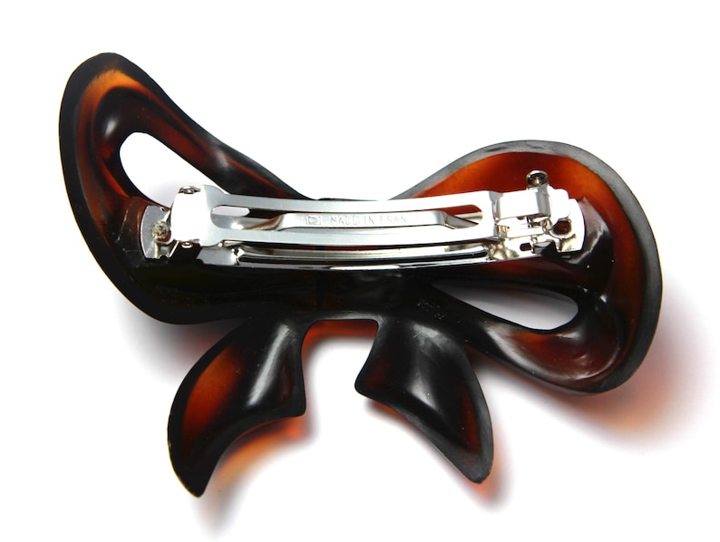 May include: A brown plastic hair clip shaped like a bow with a silver metal clasp. The clasp has the words "Made in Japan" engraved on it.