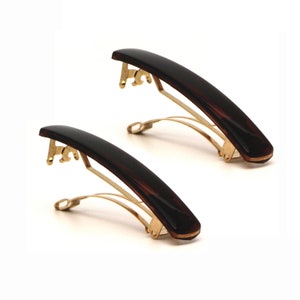 May include: Two brown tortoiseshell hair clips with gold metal clasps. The clips are curved and have a smooth, glossy finish.