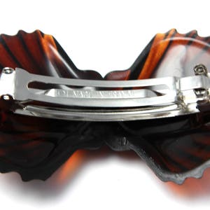 May include: A brown tortoiseshell hair clip with a scalloped edge and a silver metal clasp. The clip is shaped like a butterfly.
