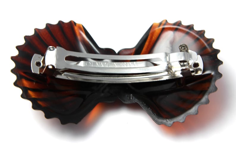 May include: A brown tortoiseshell hair clip with a scalloped edge and a silver metal clasp. The clip is shaped like a butterfly.