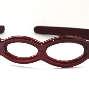 May include: A burgundy plastic headband with a decorative design of connected oval cutouts.