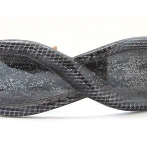 May include: A black infinity-shaped hair clip with a textured surface and a glittery finish.