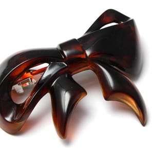 May include: A brown plastic hair clip shaped like a bow. The clip has a metal clasp.