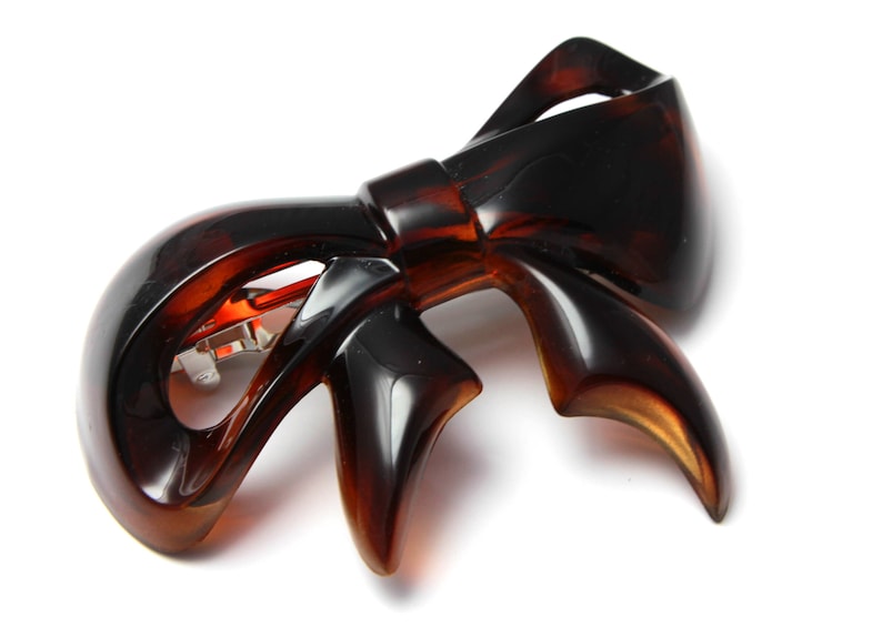 May include: A brown plastic hair clip shaped like a bow. The clip has a metal clasp.