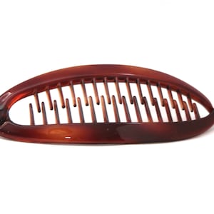 May include: A brown plastic hair claw with a comb design. The claw is shaped like a half-circle and has a smooth, glossy finish.
