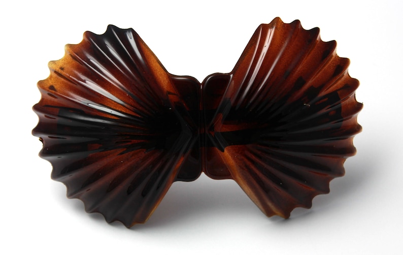 May include: A brown plastic hair clip shaped like two seashells. The clip is closed and ready to hold hair.