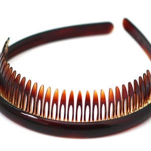 Puede incluir: Una diadema de plástico marrón con una fila de dientes a lo largo del borde inferior. La diadema está diseñada para sujetar el cabello en su lugar.