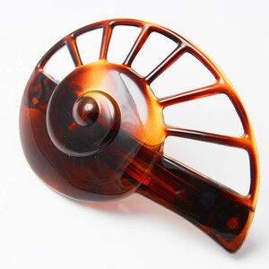 May include: A brown tortoise shell hair clip with a fan-shaped design. The clip has a spiral detail in the center.