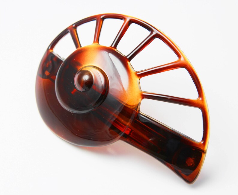 May include: A brown tortoise shell hair clip with a fan-shaped design. The clip has a spiral detail in the center.