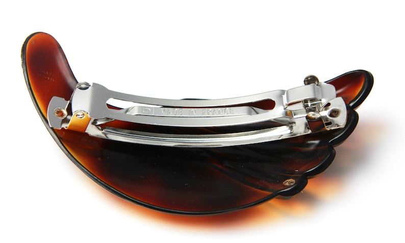 May include: A brown tortoiseshell hair clip with a silver metal clasp. The clip is shaped like a half-circle and has a textured surface.