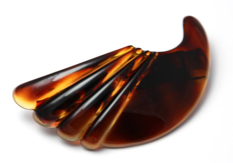 May include: A brown tortoiseshell hair clip with a fan-shaped design. The clip is made of plastic and has a smooth, glossy finish.