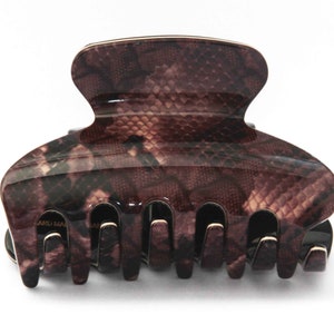 May include: A large, brown and black hair claw clip with a snakeskin pattern. The claw clip is made of glossy, durable material and features a secure grip design. The clip is ideal for holding thick hair in place.