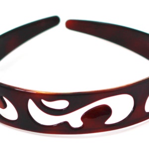 Può includere: Una fascia per capelli marrone tartarugata con un design decorativo traforato. La fascia è realizzata in un materiale lucido e presenta una serie di forme curve e aperte sul davanti.