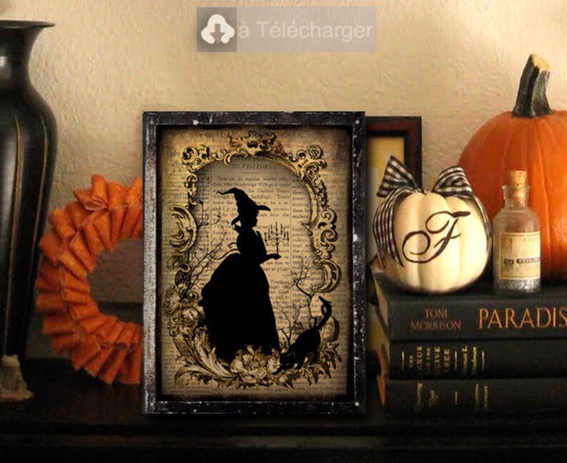 May include: A framed print of a black silhouette of a witch holding a candlestick in front of a vintage book page with ornate floral designs. The print is in a black frame and is sitting on a shelf with other decorative items.