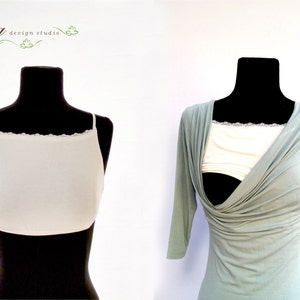 Puede incluir: Dos maniqu&iacute;es llevan blusas blancas y verde claro. La blusa blanca tiene un borde de encaje y es un sujetador de lactancia. La blusa verde claro es una blusa de lactancia con un dise&ntilde;o de envoltura. El texto "Te'ena design studio" es visible en la esquina superior izquierda de la imagen.