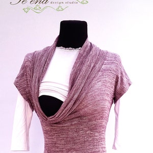 Puede incluir: Una blusa de punto color malva con cuello de pico y mangas cortas. La blusa está superpuesta sobre una camiseta blanca.