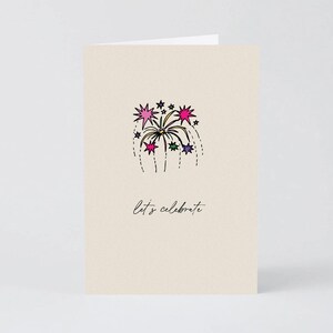 May include: A cream-coloured greeting card featuring a hand-drawn illustration of a colourful firework burst in shades of pink, purple, and green. Below the firework, the text "let's celebrate" is written in a simple, black, cursive script font.