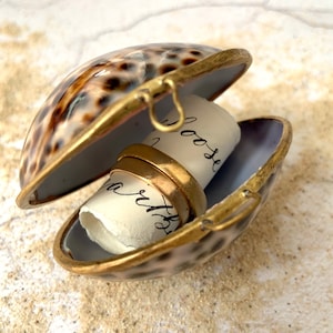 May include: A seashell ring box with a brass latch, open to reveal two gold wedding bands and a rolled piece of paper with the words "loose" and "worth" written on it.
