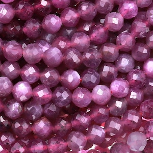 May include: A strand of pink faceted gemstone beads. The beads are round and have a smooth, polished finish.
