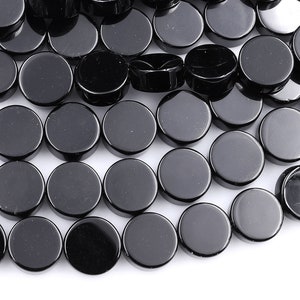 May include: A close-up of a pile of black round beads. The beads are smooth and shiny, and they are arranged in a random pattern.