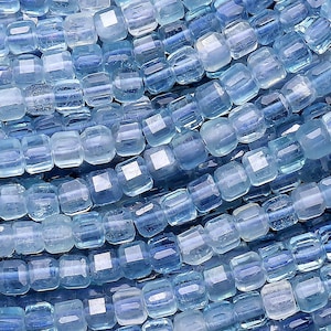 Puede incluir: Una hebra de cuentas de piedra preciosa de aguamarina azul claro. Las cuentas son facetadas y tienen forma cuadrada. Las cuentas están enhebradas en un hilo transparente.