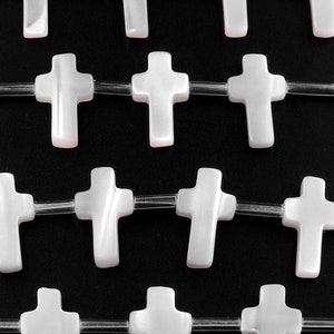May include: A strand of white mother of pearl cross beads on a clear elastic cord. The cross beads are strung in a repeating pattern.