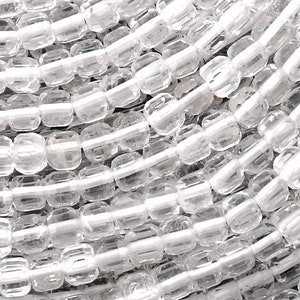 Puede incluir: Una hebra de cuentas de cristal transparentes, facetadas y de forma cuadrada. Las cuentas están enhebradas en un hilo blanco y están dispuestas en un patrón circular.