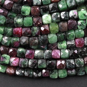 Może przedstawiać: Szereg zielonych, czarnych i czerwonych koralików z kamieni szlachetnych. Koraliki są fasetowane i mają kwadratowy kształt.