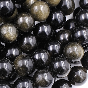 May include: A strand of black and gold gemstone beads. The beads are round and have a smooth, polished finish. The gold flecks in the beads are visible and add a touch of sparkle.
