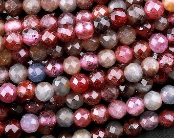 May include: A strand of faceted gemstone beads in shades of pink, red, and purple. The beads are round and have a slightly irregular shape.