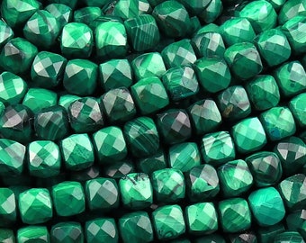 May include: A strand of green malachite beads, each bead is faceted and has a square shape.