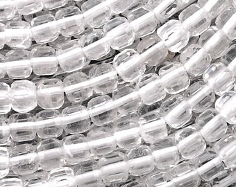 May include: A strand of clear, faceted, square-shaped crystal beads. The beads are strung on a white thread and are arranged in a circular pattern.