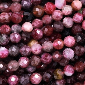 Może przedstawiać: Szereg fasetowanych koralików z kamieni szlachetnych w odcieniach różowego, czerwonego i brązowego. Koraliki są okrągłe i mają lekko nieregularny kształt.