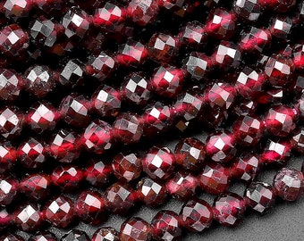 May include: A strand of deep red garnet beads, each bead is faceted and has a slightly irregular shape. The beads are strung together to create a long, continuous strand.