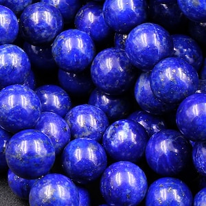 May include: A close-up of a strand of round, blue lapis lazuli beads. The beads are smooth and have a slightly metallic sheen. The beads are arranged in a random pattern, creating a visually appealing texture.