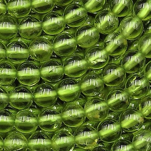 May include: Close-up of a collection of round, translucent, olive-green beads. The beads are arranged closely together, filling the frame. The beads have a glossy finish, reflecting light and creating a textured appearance. Ideal for jewelry making.